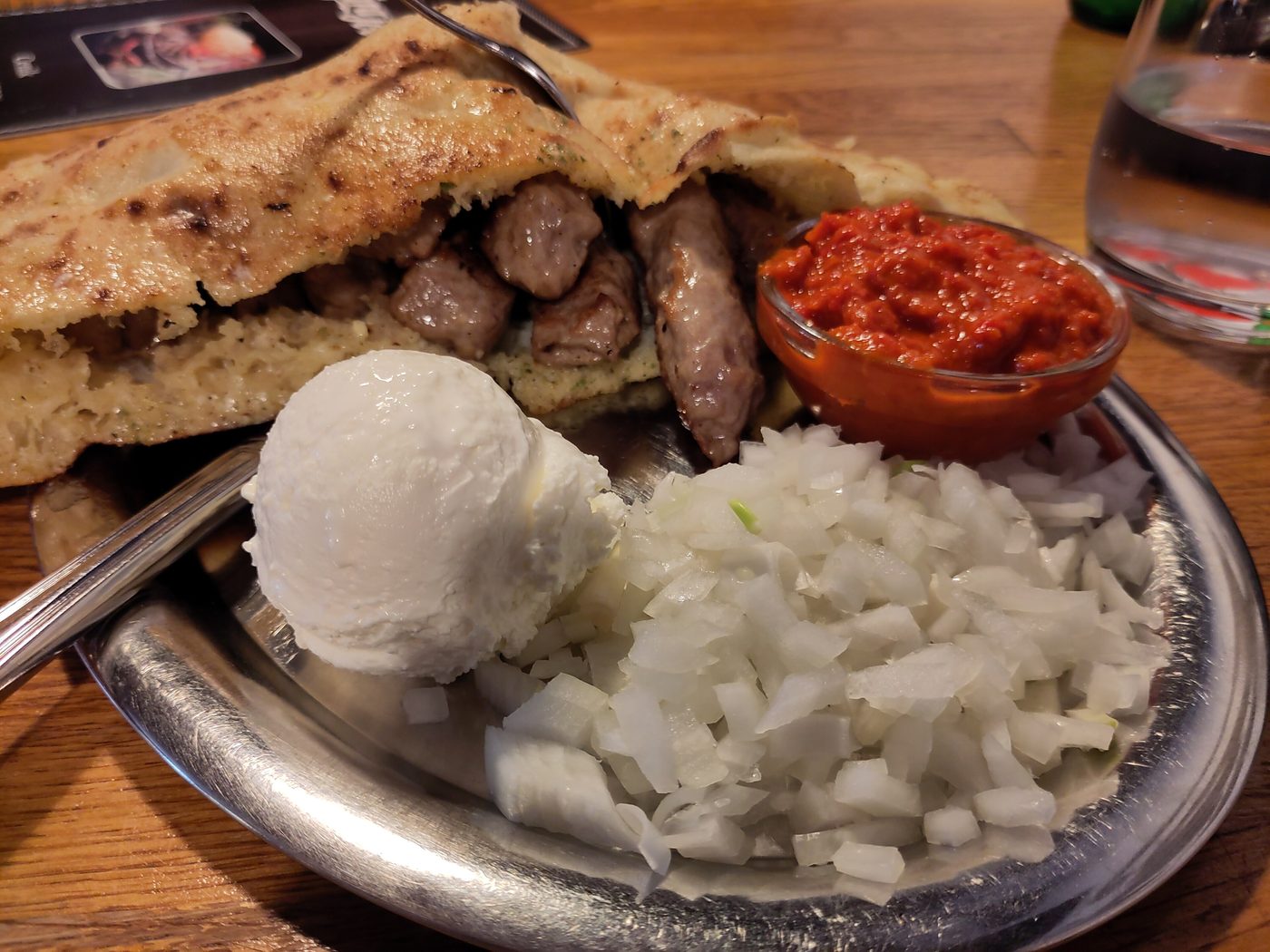 Ćevapi in flatbread with kajmak, chopped onion and ajvar on a metal plate