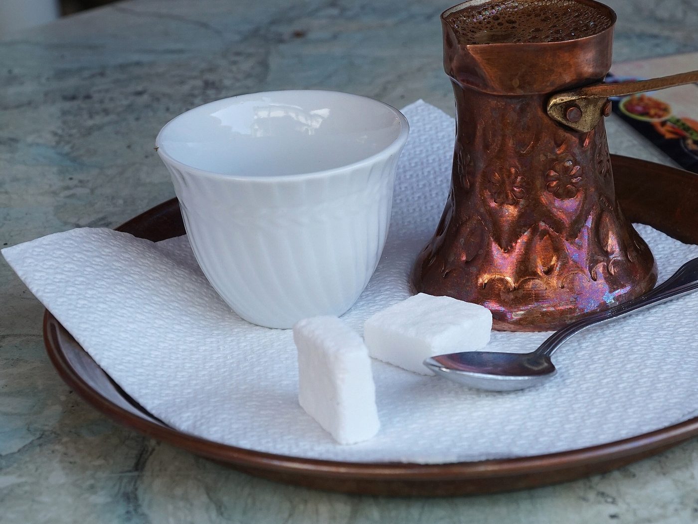 A copper džezva of coffee with a small white cup and sugar cubes